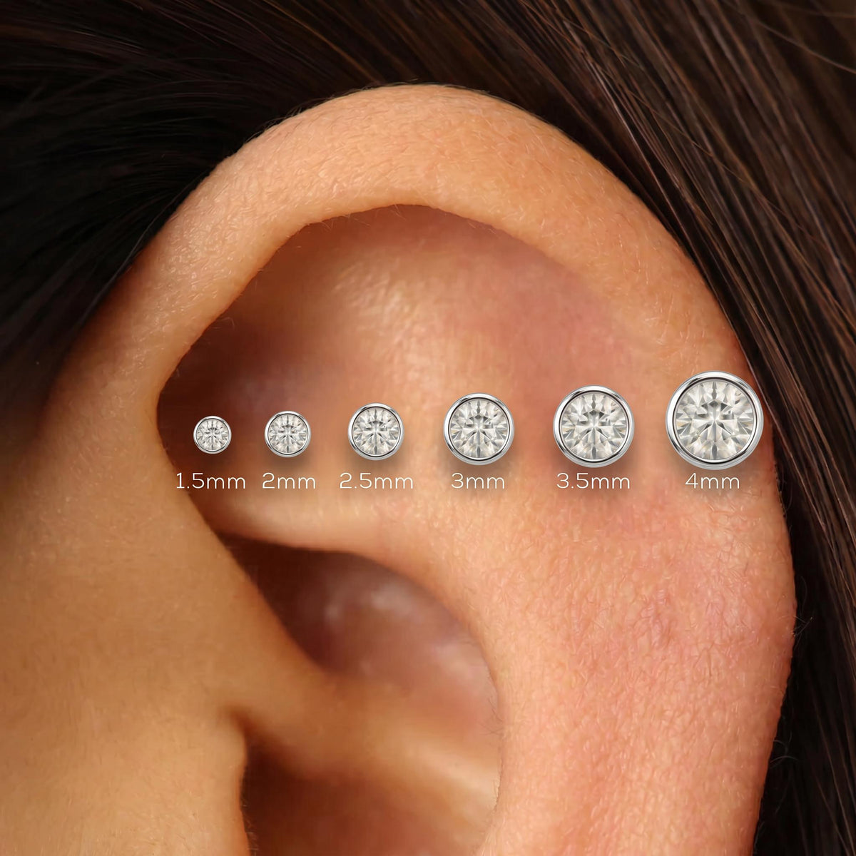 a close-up of a person's ear with five diamond studs of varying sizes, ranging from 1.5mm to 3.5mm, indicating the different sizes available for earrings.