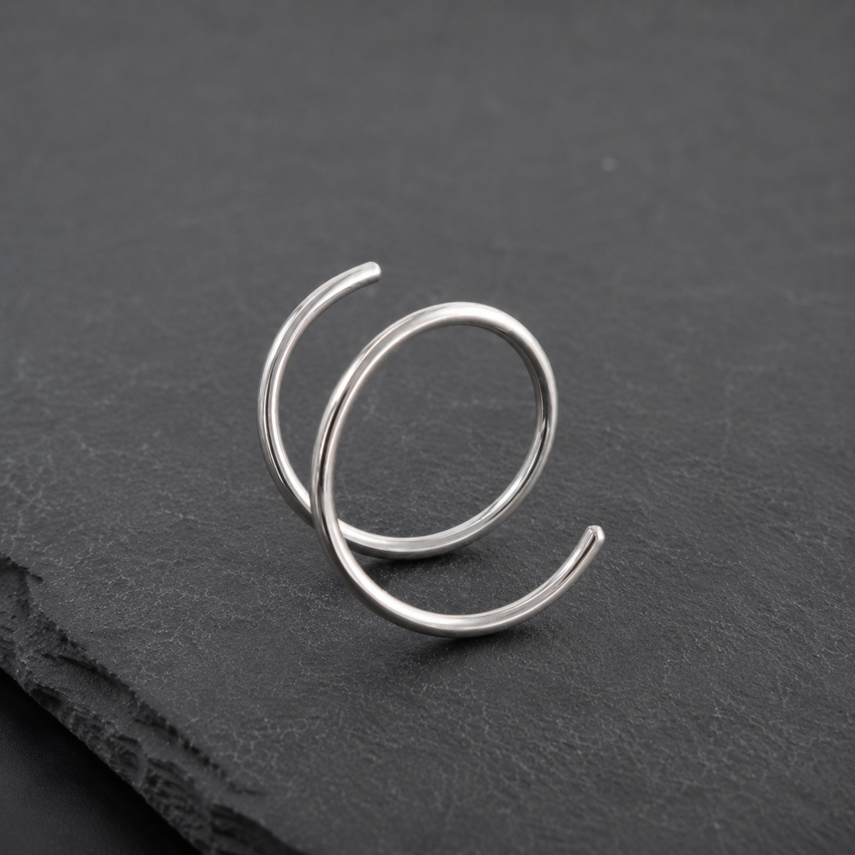 A silver ring with a twisted, spiral design is resting on a dark surface.
