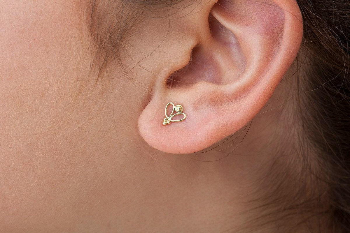 A close-up view of a person's ear with a small gold earring featuring a butterfly design.