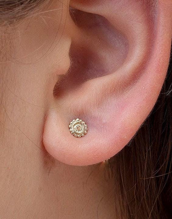 Sun Stud Earrings: A close-up view of a person's ear, showing a small gold-colored earring with a decorative design.