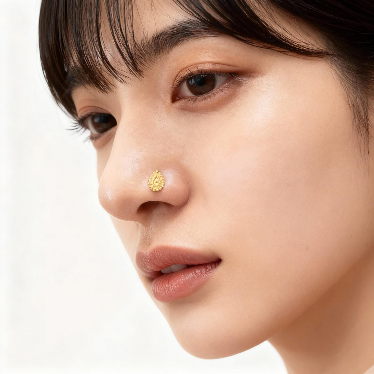 A close-up portrait of a young woman with dark hair and a gold nose stud.