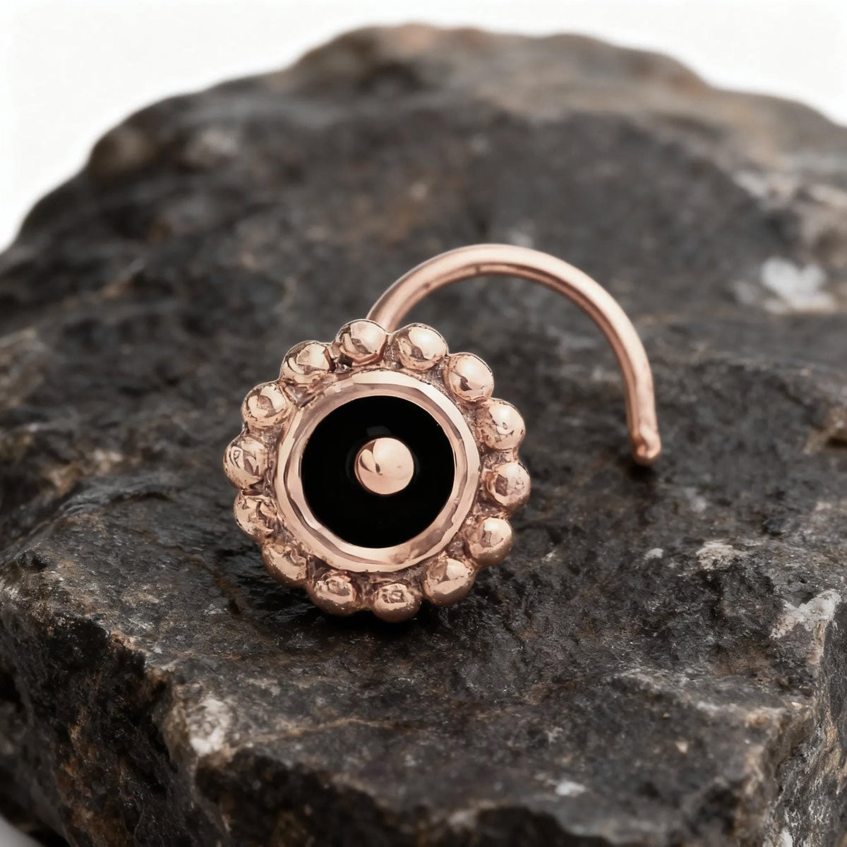 A copper-colored nose ring with a black center is resting on a dark, rocky surface.