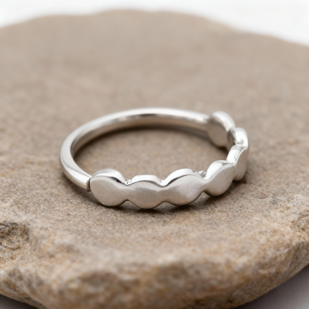A silver ring with a unique design sits on a rock.
