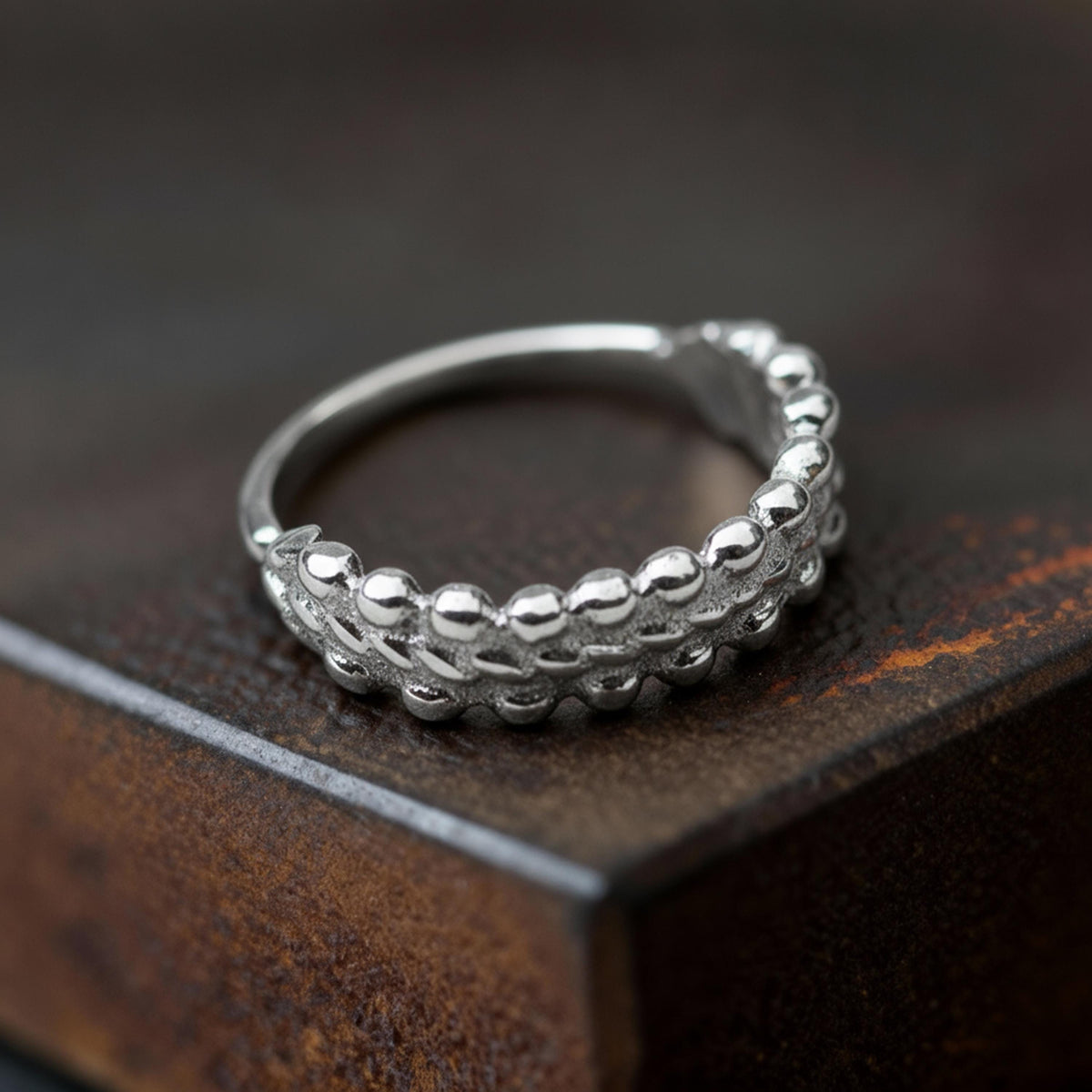 A silver ring with a unique, textured design sits on a dark, textured surface.