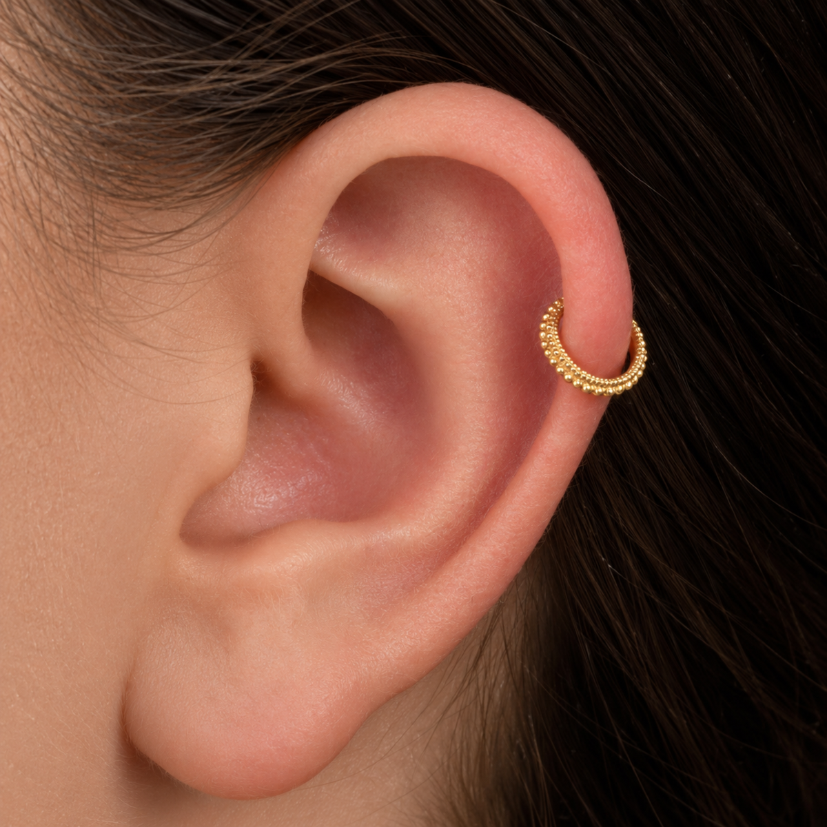 A close-up view of a person's ear with a gold-colored earring in the earlobe.