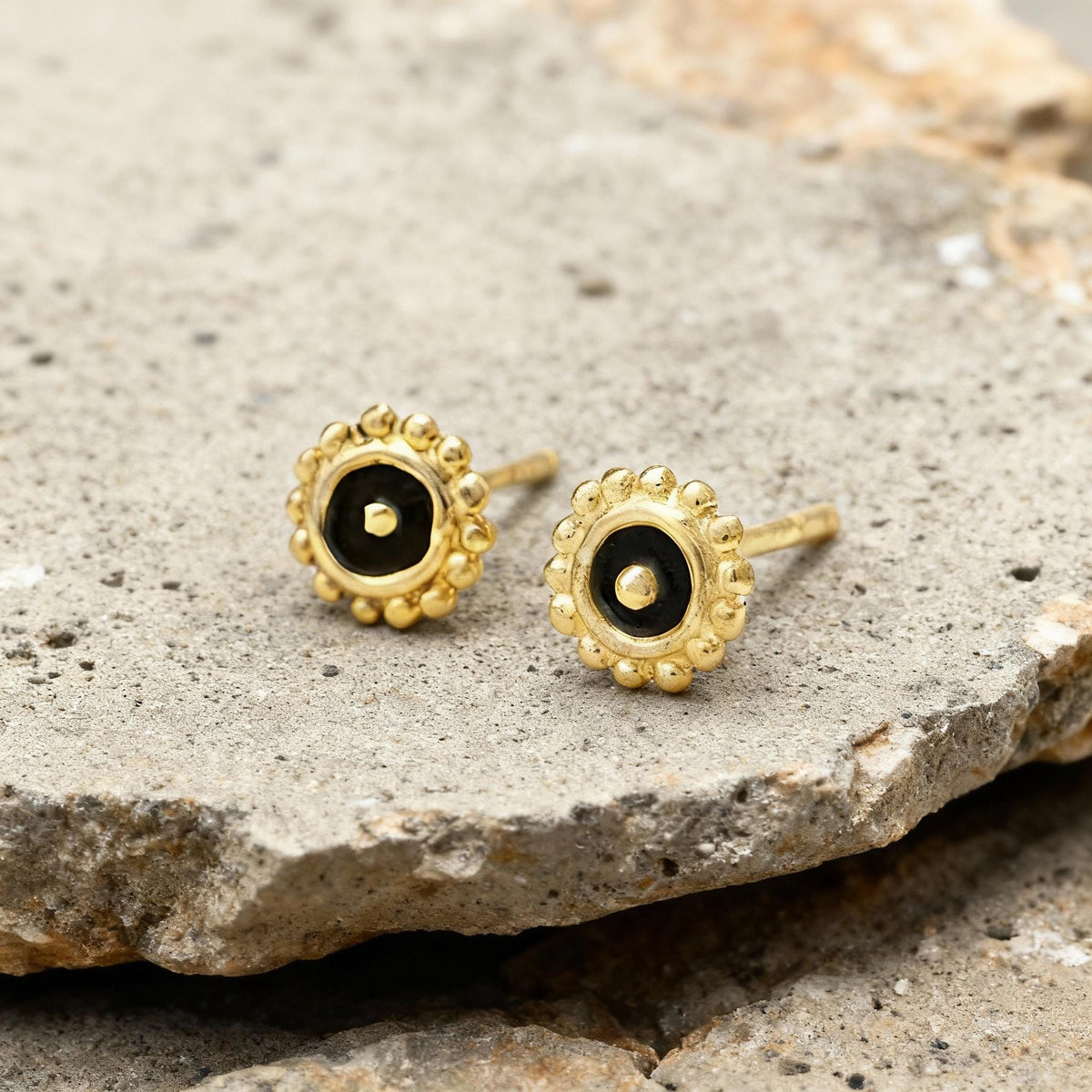 A pair of gold earrings with black stones on a rock surface.