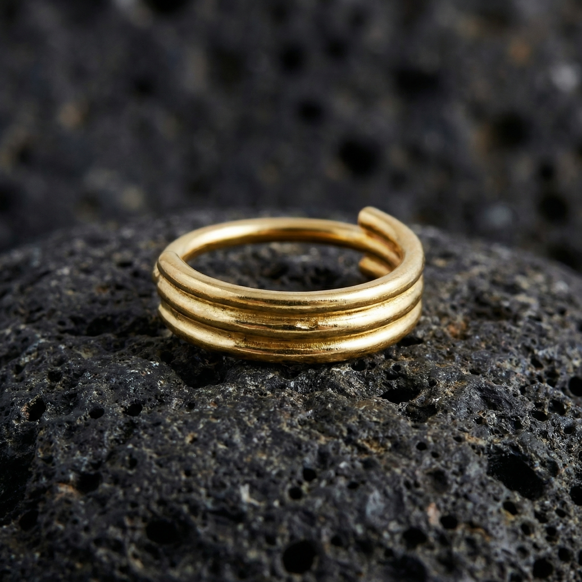 A gold ring with three concentric bands is resting on a dark, rocky surface.