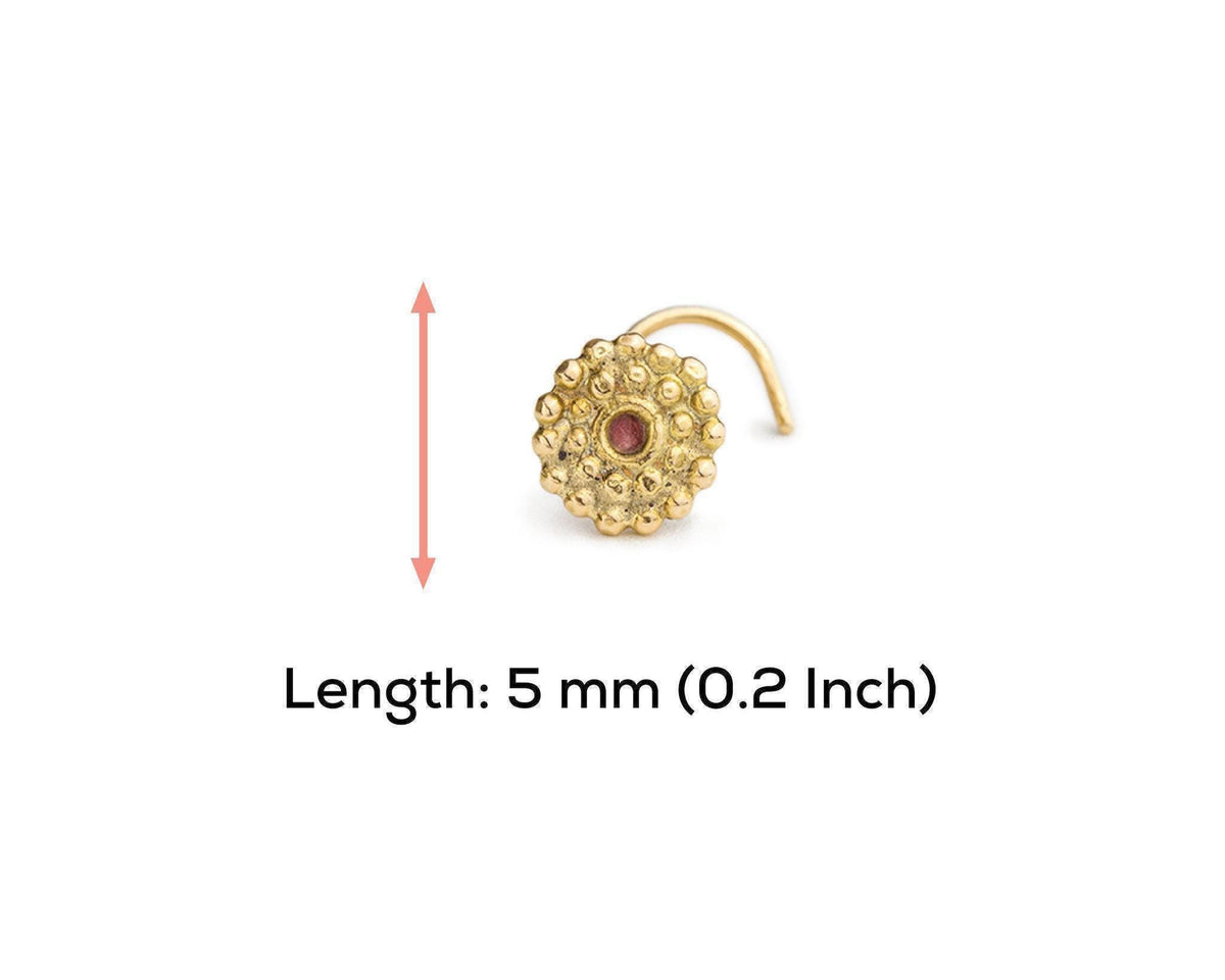 A gold-colored nose ring with a red gemstone is shown against a white background.