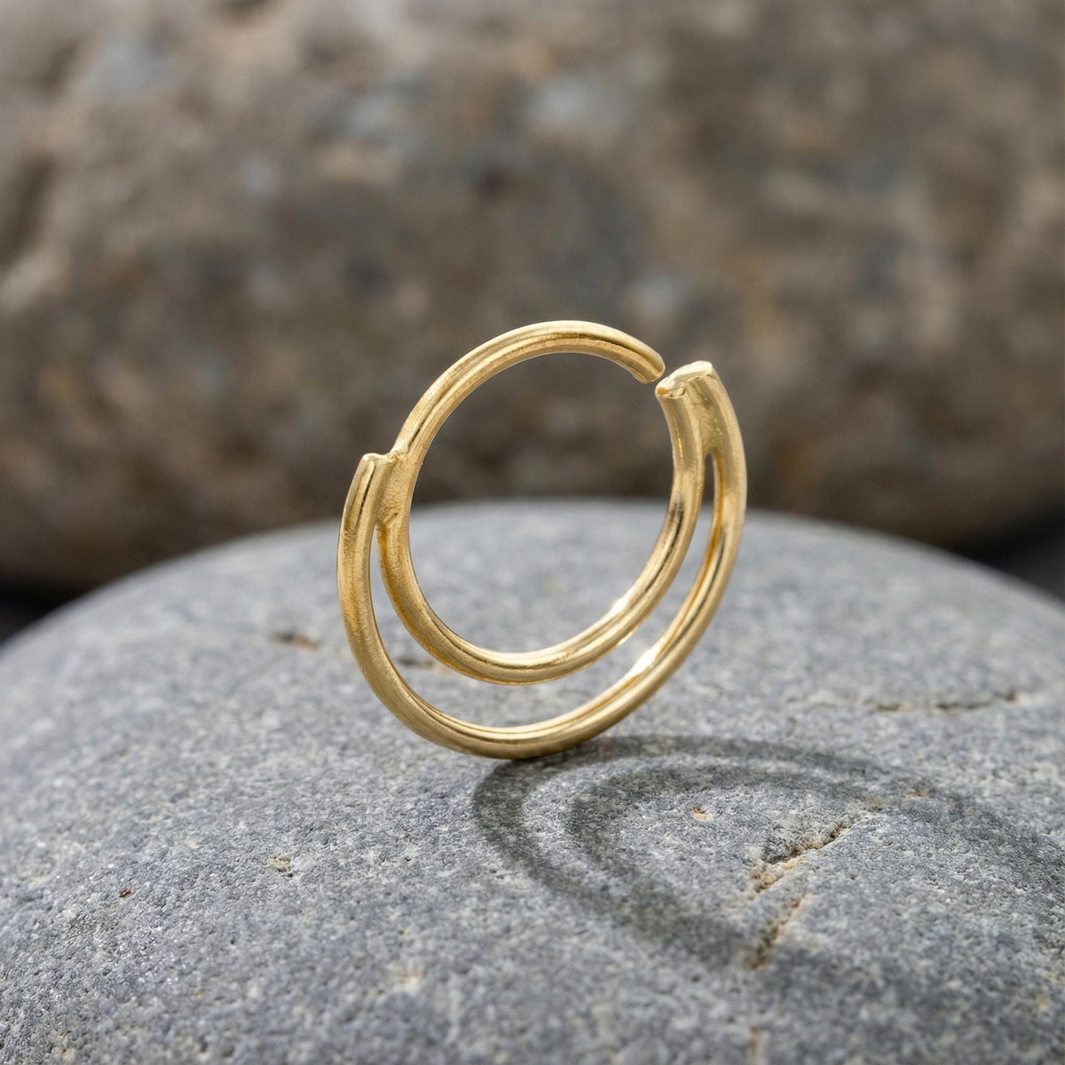 A gold ring with a unique design sits on a gray rock.