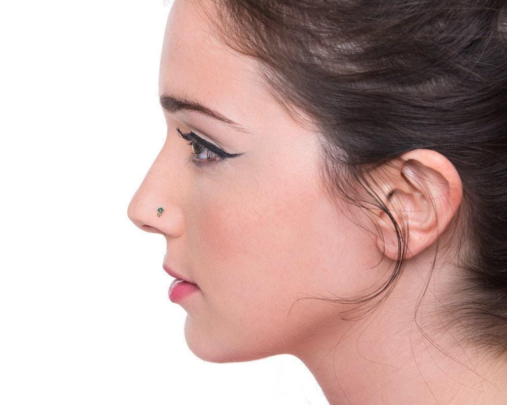 A close-up profile view of a woman with dark hair, wearing a nose stud.