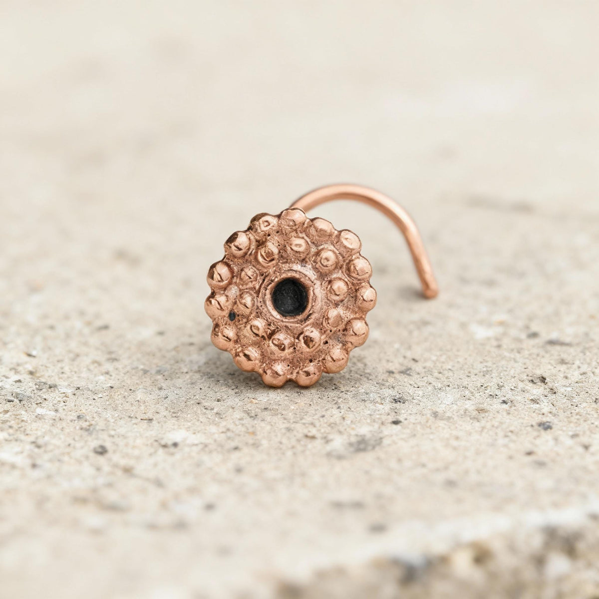 A copper-colored metal nose ring with a small hole in the center is resting on a concrete surface.