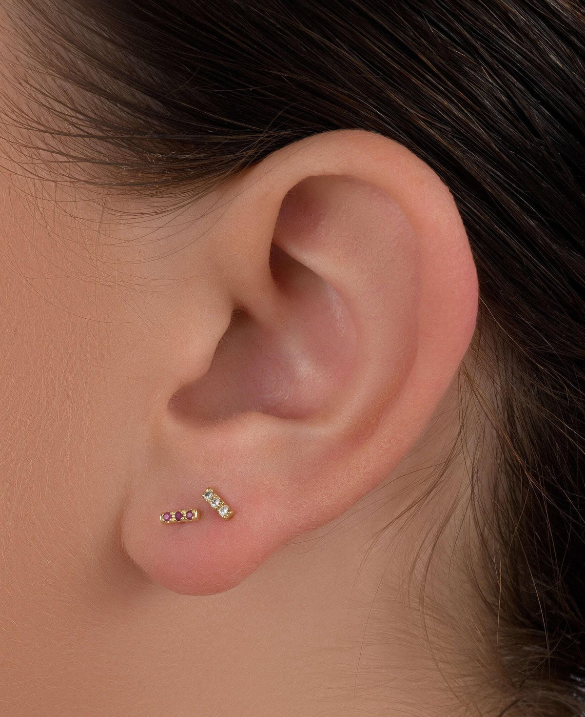 a close-up view of a person's ear with two small gold earrings with gemstones inserted.