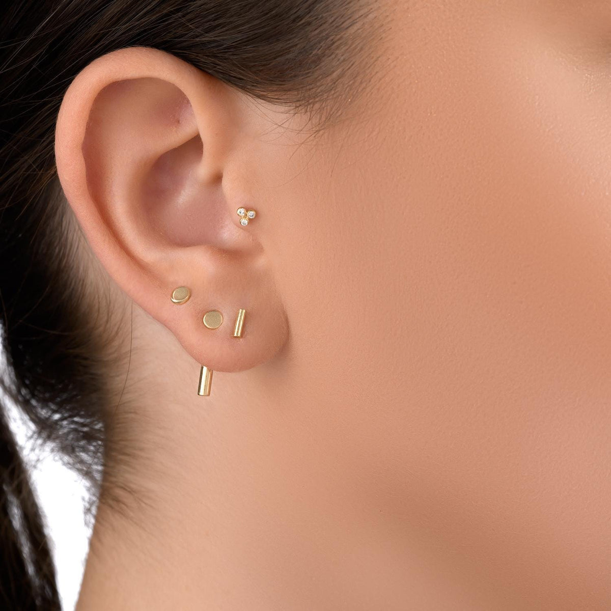 A close-up view of a person's ear adorned with three small gold earrings.
