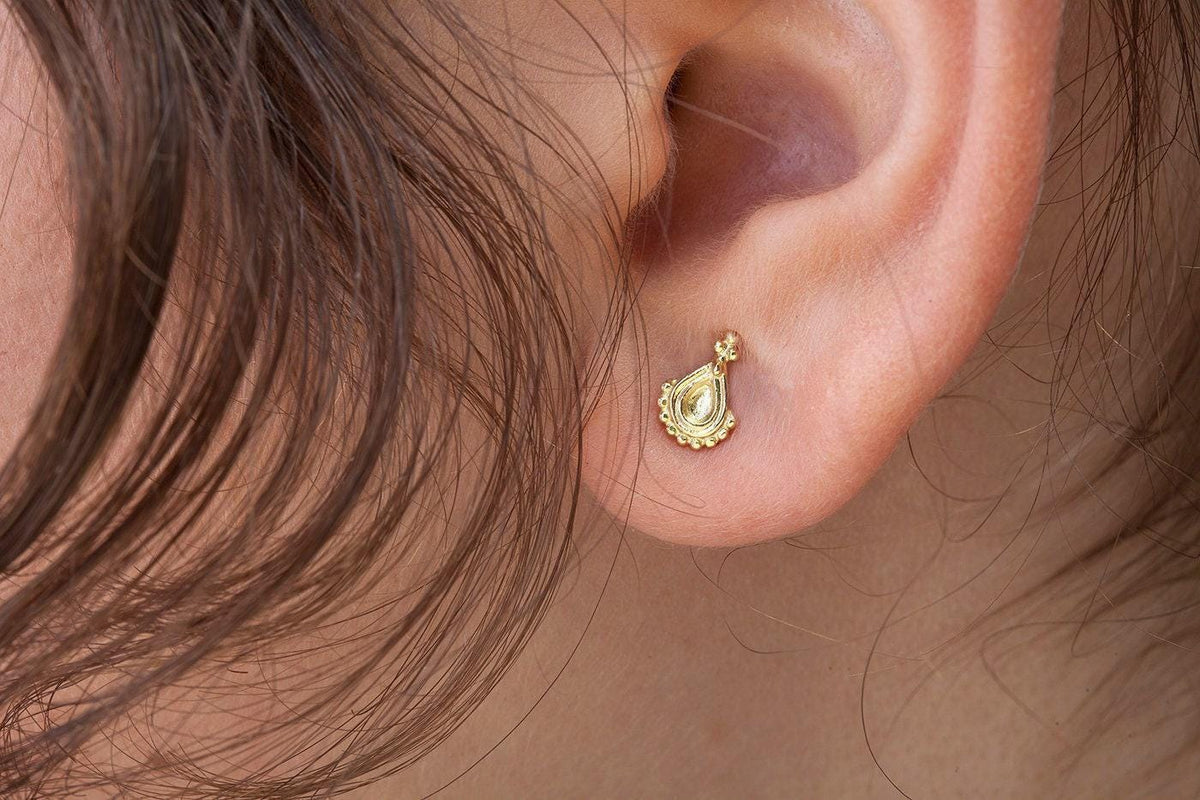 A close-up view of a person's ear adorned with a small gold earring featuring a delicate floral design.