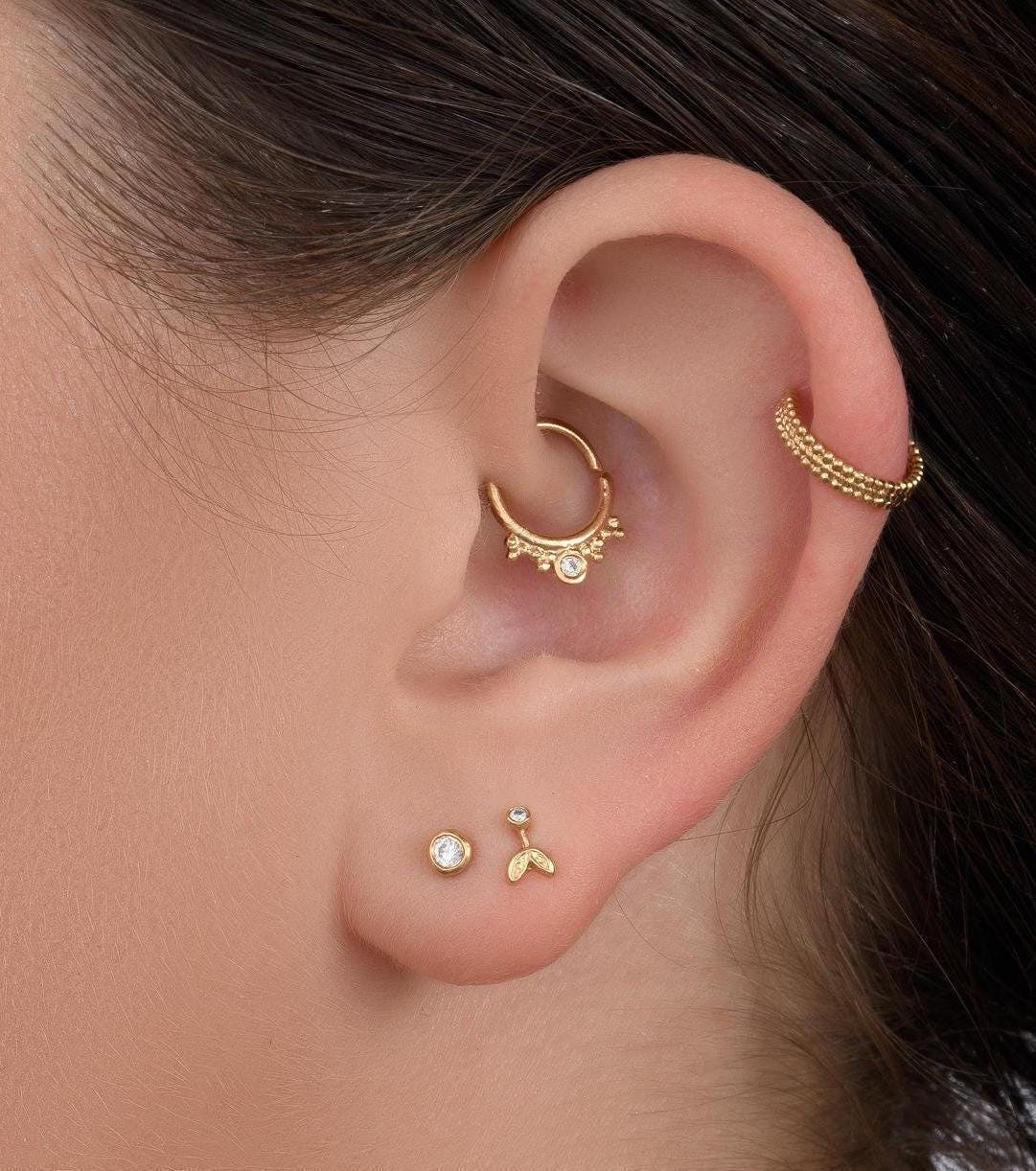 a close-up view of a person's ear adorned with multiple gold earrings, including a ring and a small earring.