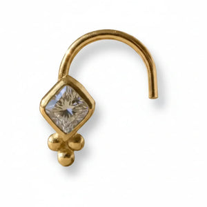 A silver nose ring with a diamond-shaped gemstone is displayed on a wooden surface.