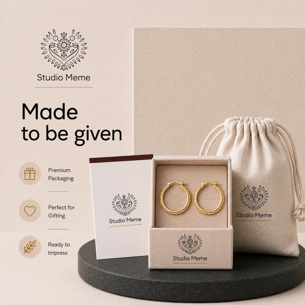 a pair of gold earrings displayed in a box, accompanied by a beige drawstring bag and a premium packaging box. The earrings are presented in a studio meme-inspired packaging design, which includes a logo and text that reads "Made to be given".