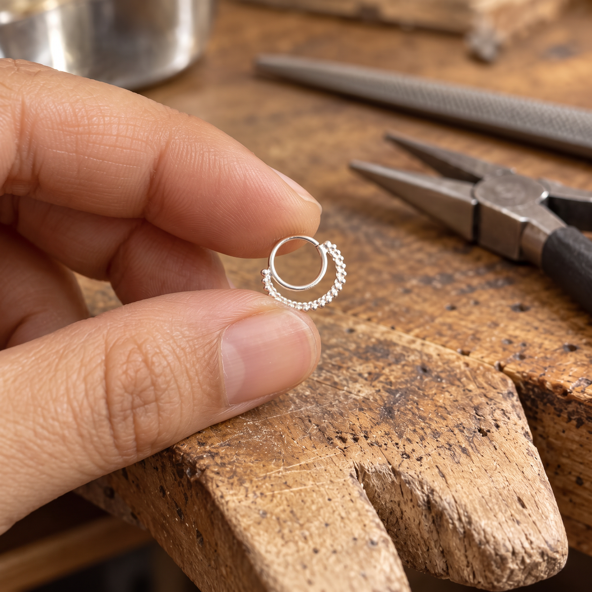 A hand holding a small silver ring with a spiral design on a wooden workbench.