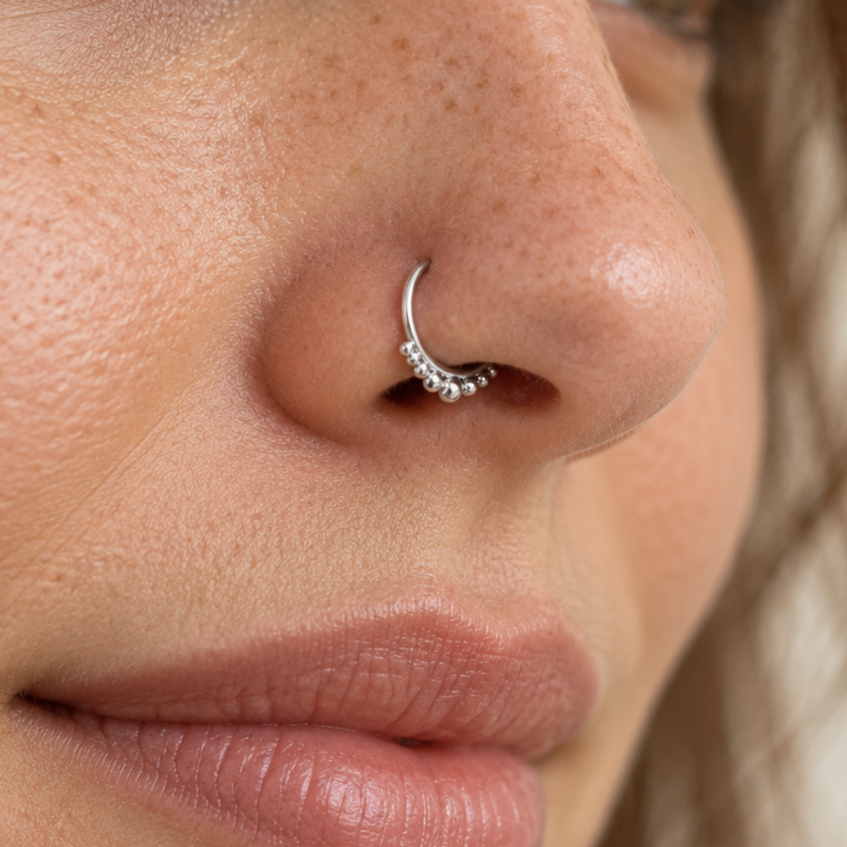 A close-up of a person's nose and mouth, with a silver nose ring featuring small beads.