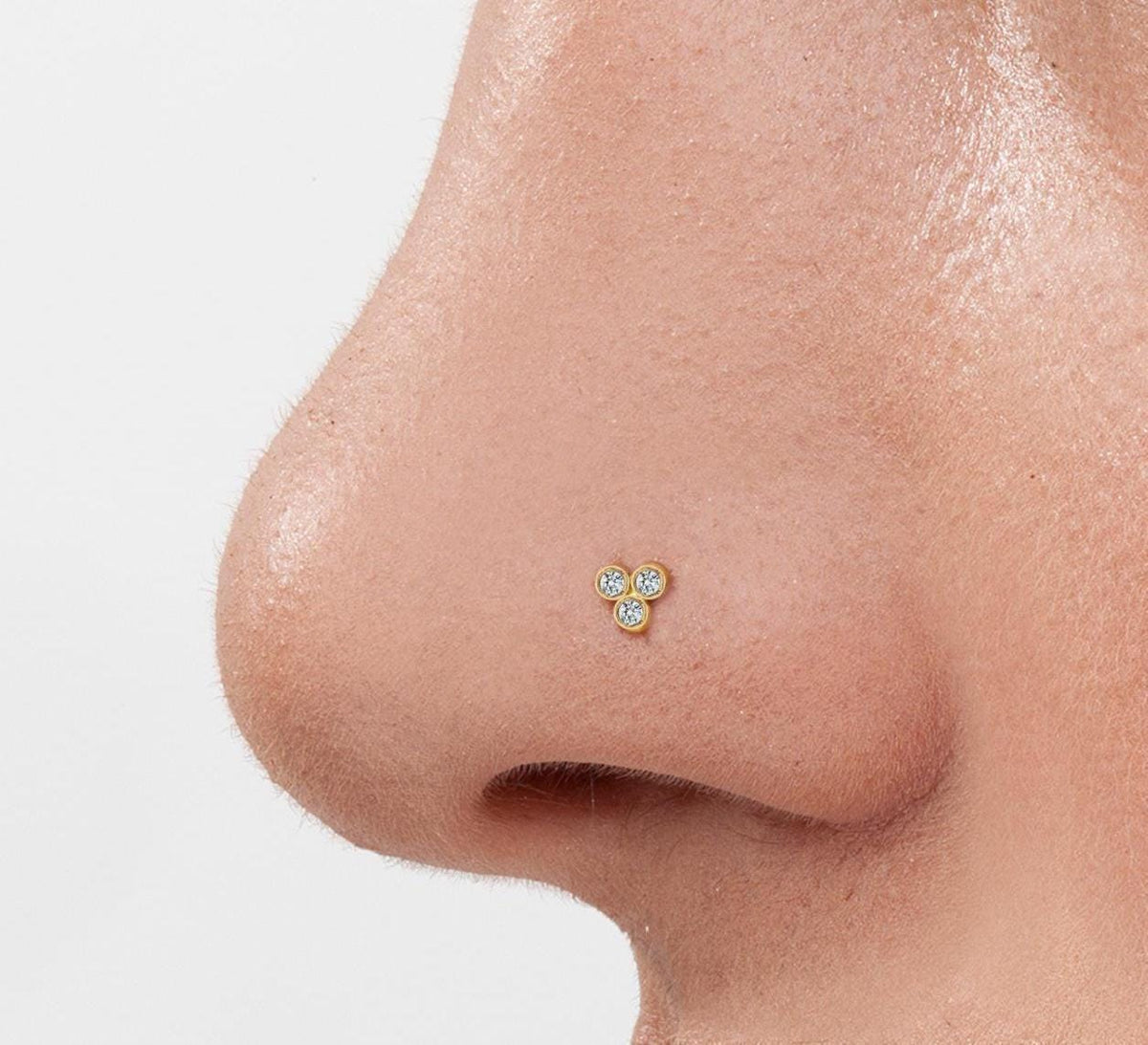 A close-up of a person's nose with a small, three-stone nose stud.
