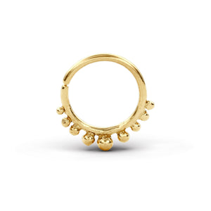 A gold-colored ring with a decorative design, featuring a central ring shape with small balls or beads hanging from it.