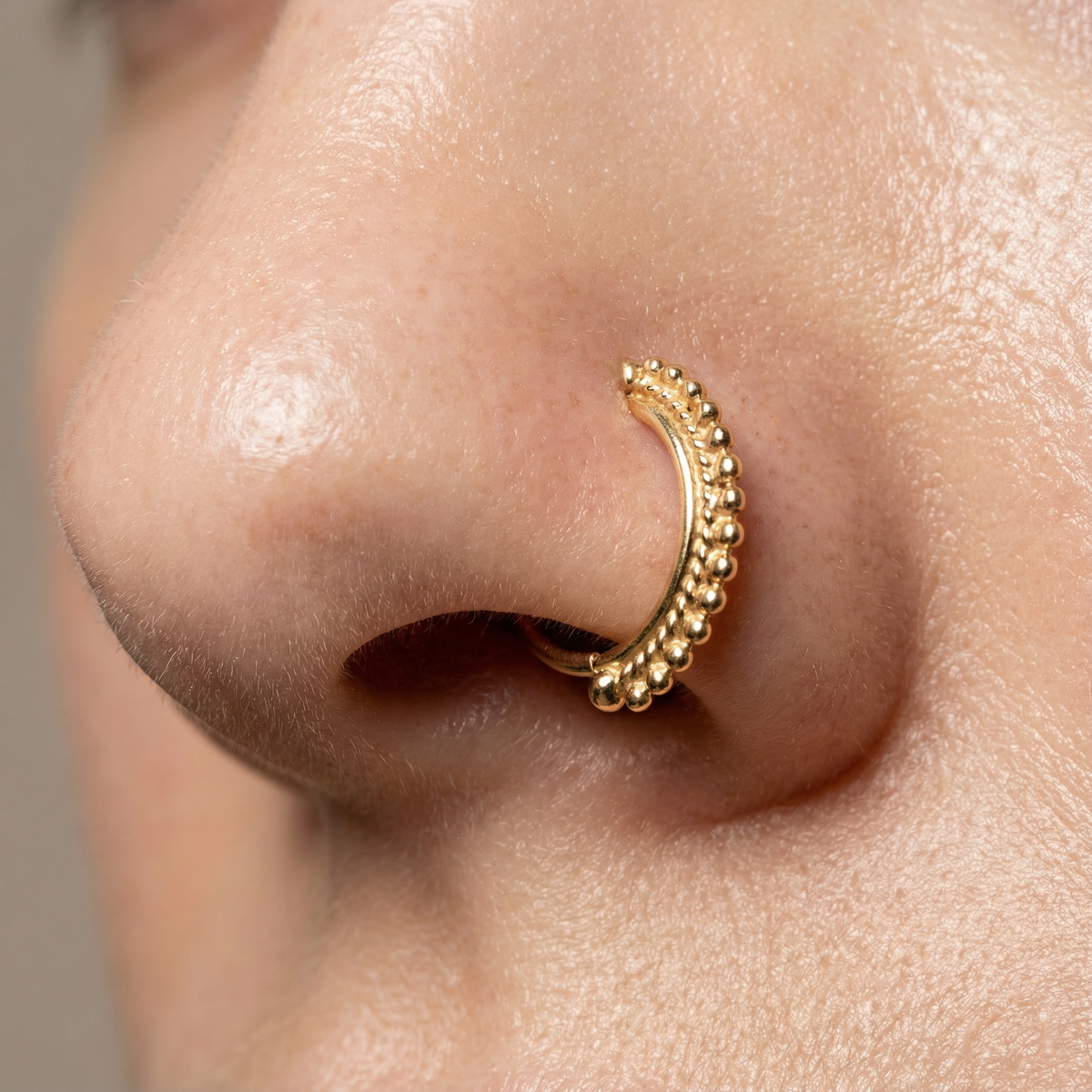 A close-up of a person's nose with a gold-colored nose ring.