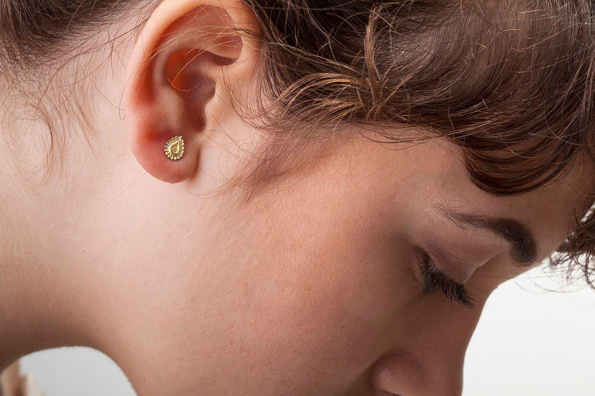 A close-up of a person's face, focusing on their ear with a small gold earring.