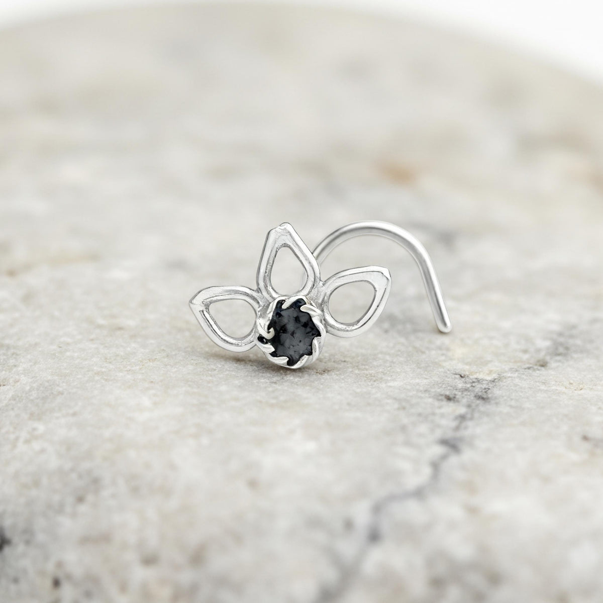 Flower Nose Stud: A silver nose ring with a black gemstone is placed on a marble surface.