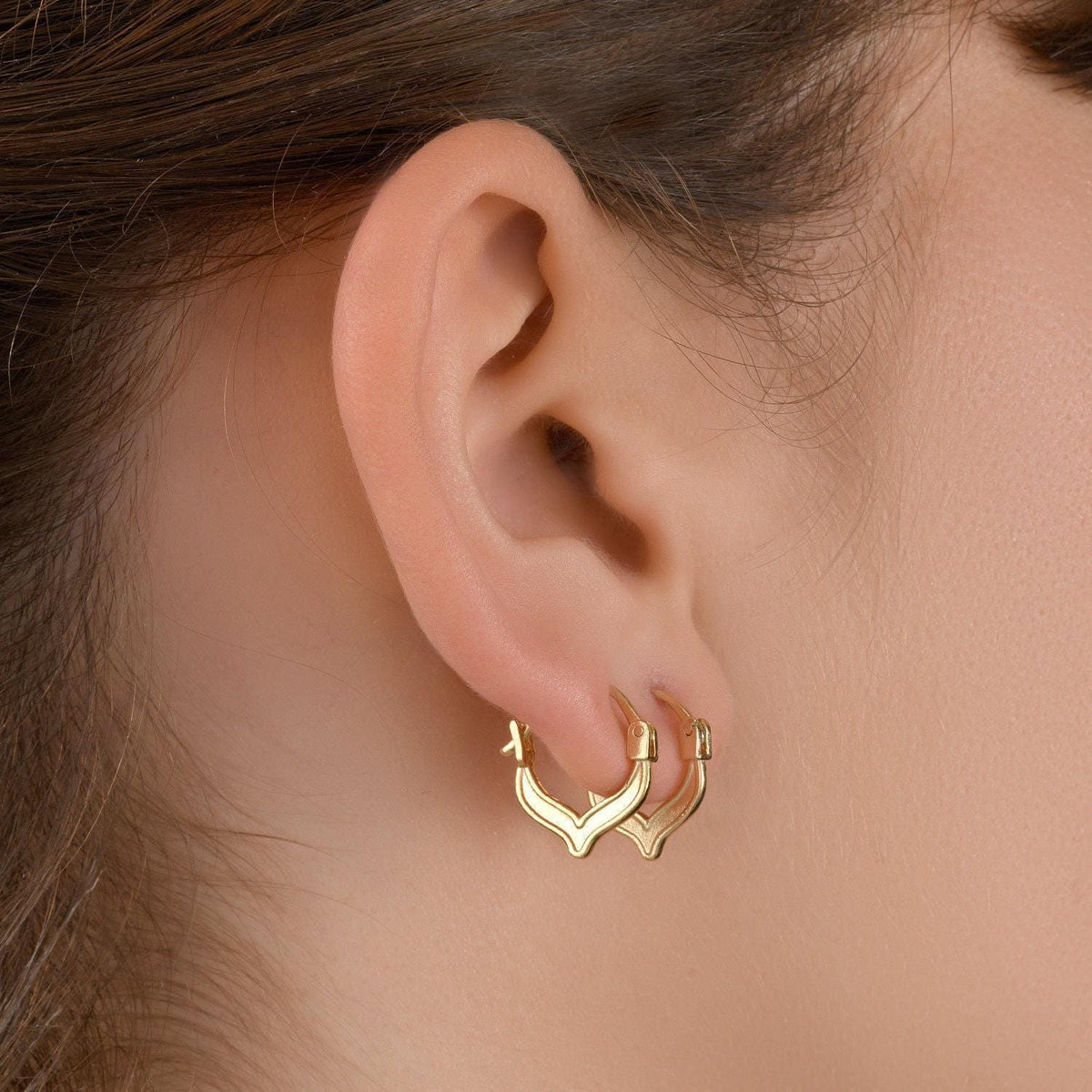 Chevron Hoop Earrings: A close-up view of a person's ear adorned with a pair of gold hoop earrings.