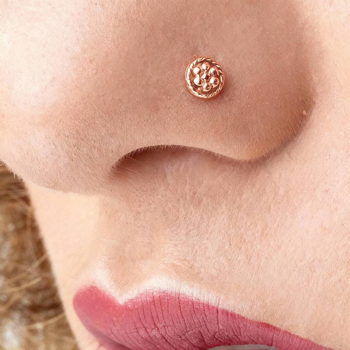 A close-up of a person's nose and lips, with a small, ornate copper-colored nose ring visible.