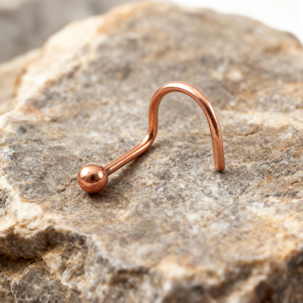 A copper-colored metal nose ring is resting on a rock.