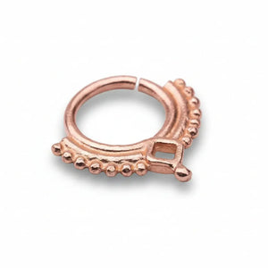 A copper-colored metal ring with a decorative design, featuring a square-shaped element and a row of small beads or dots along the edge.