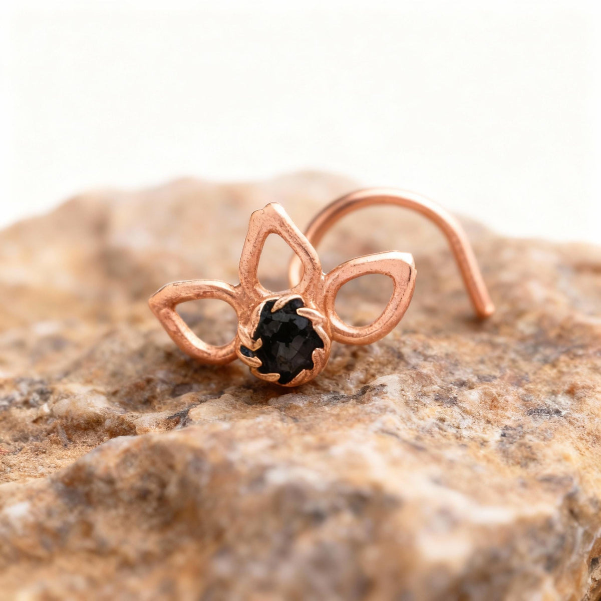 A copper-colored nose ring with a black gemstone is resting on a rock.