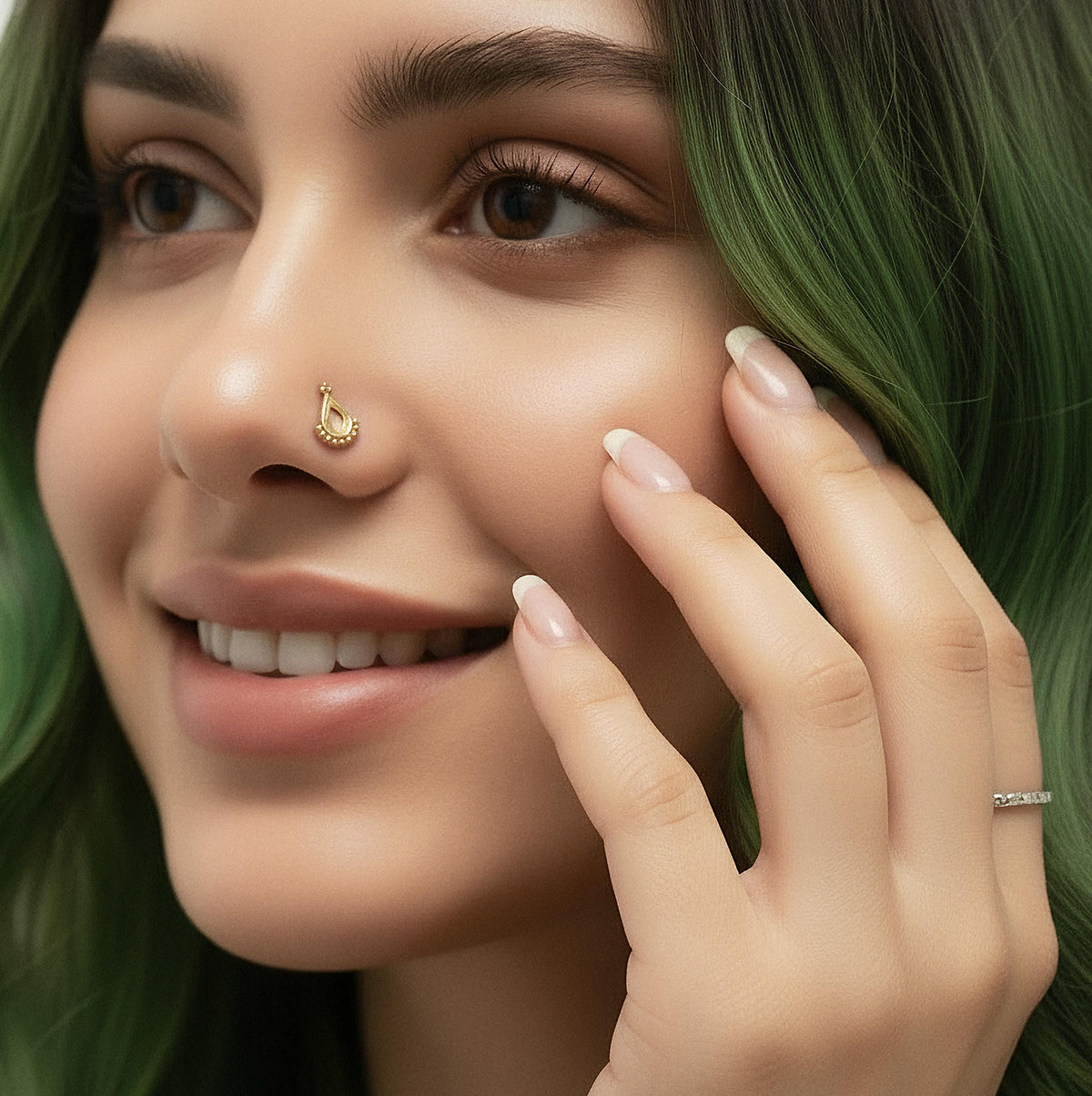 A close-up of a smiling woman with green hair and a nose piercing, wearing a ring on her finger.