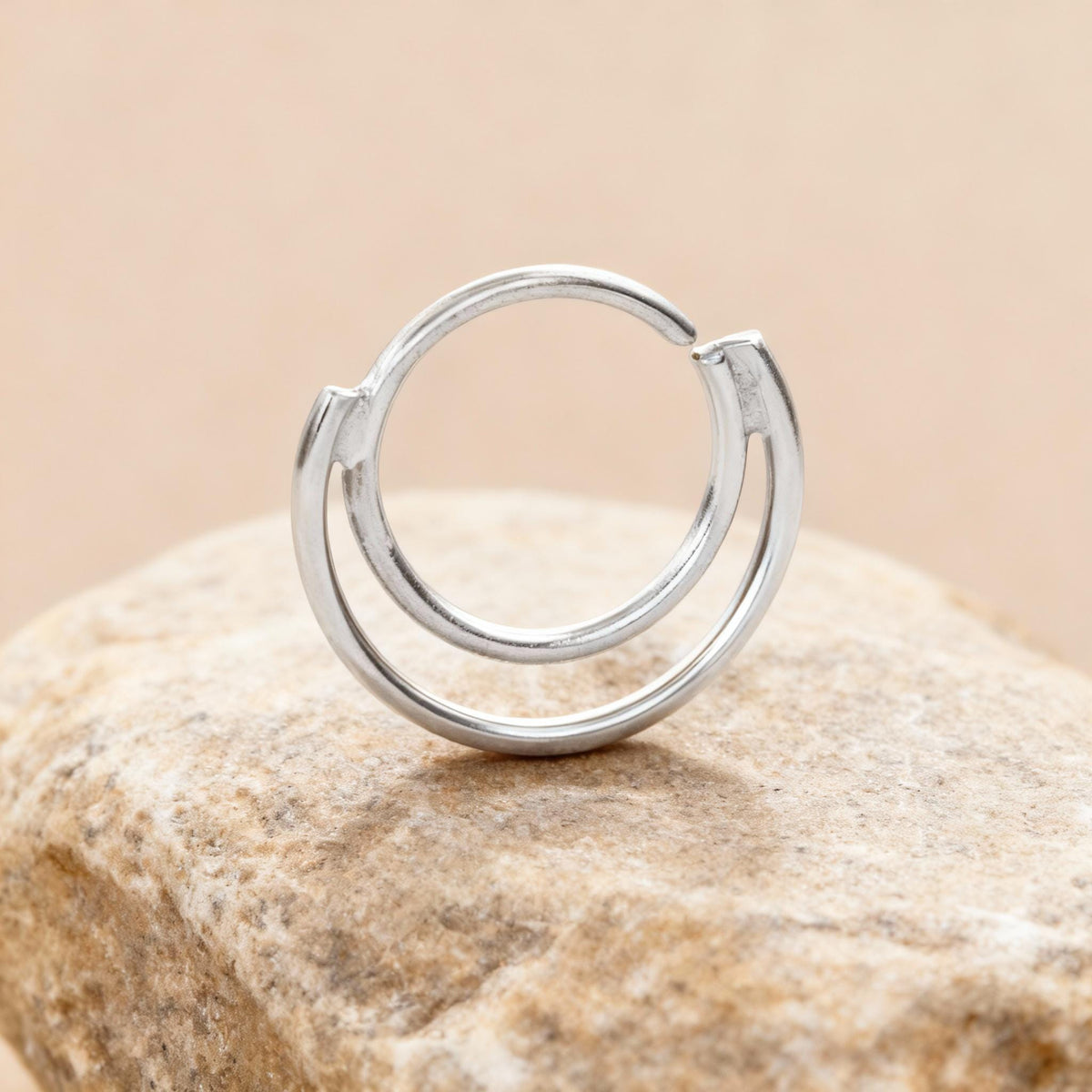 A silver ring with a circular design sits on a rock.