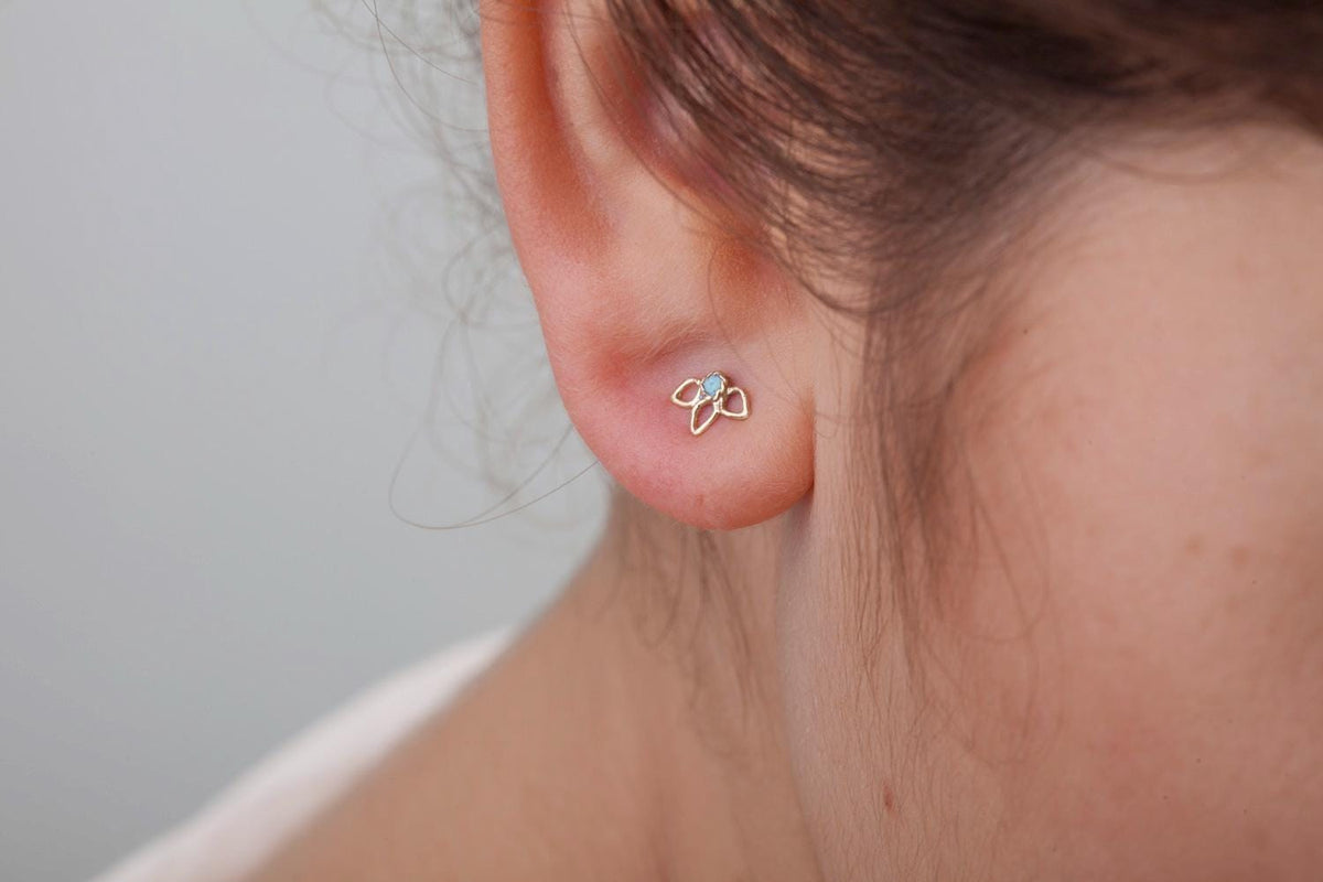 A close-up view of a person's ear, showing a delicate gold earring with a small flower design.