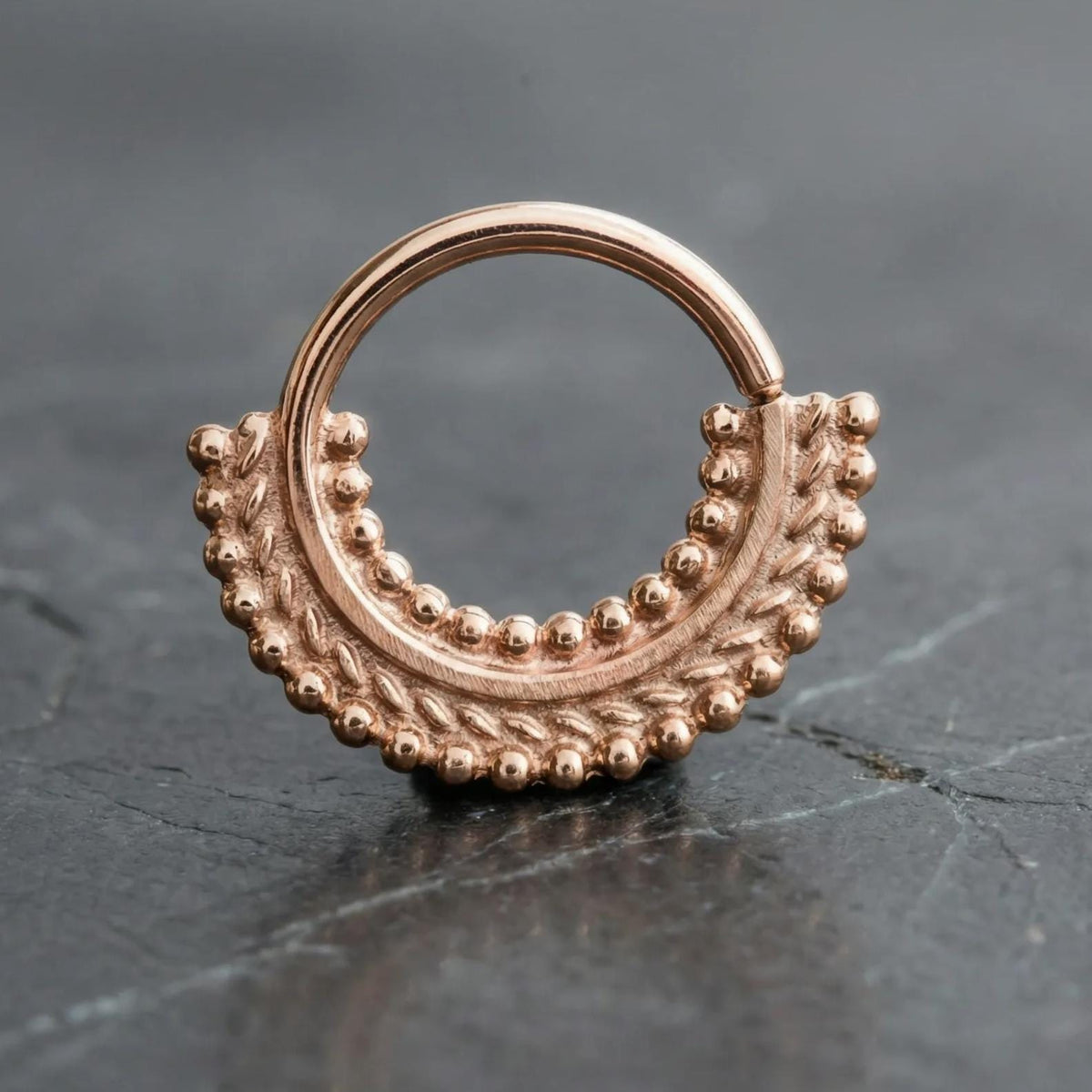 A gold-colored metal ring with a decorative design, resting on a dark surface.