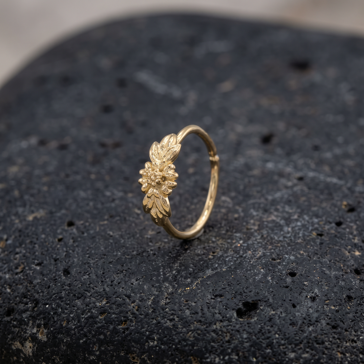 A gold-colored ring with a leaf-like design is resting on a dark, textured surface.