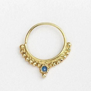 A gold-colored nose ring with a blue gemstone in the center.