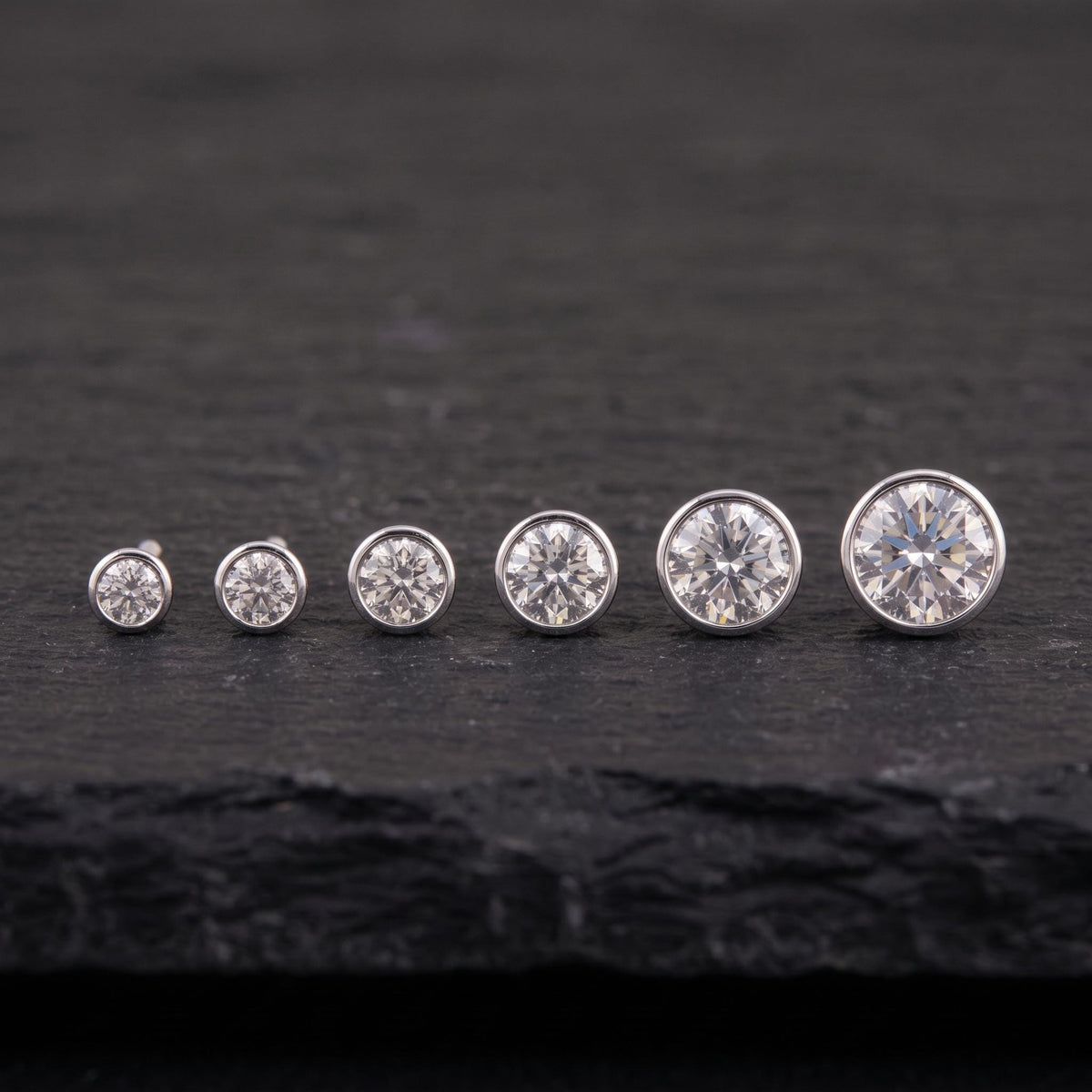 A row of six diamond earrings with varying sizes, all set against a dark background.