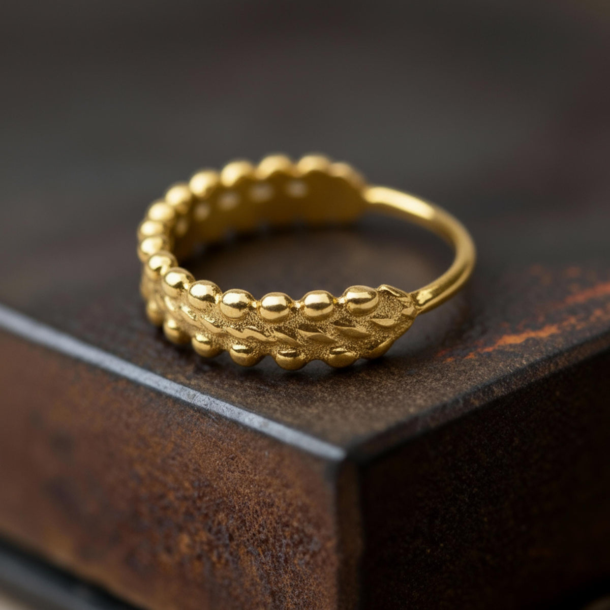 A close-up image of a gold ring with a leaf-like design on the surface it rests on.