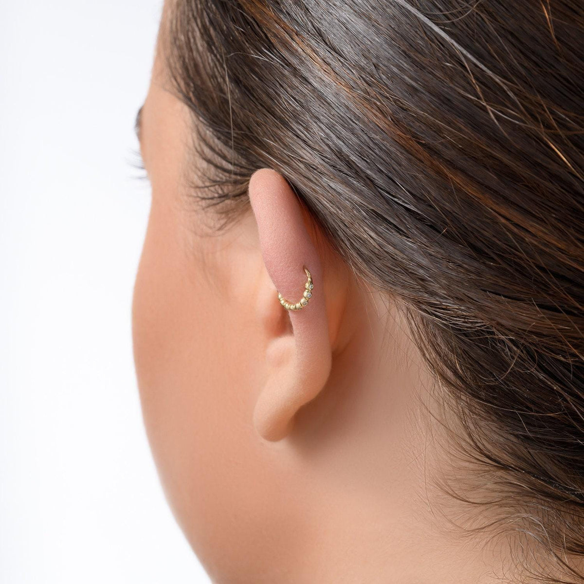 A close-up view of a person's ear with a gold hoop earring.
