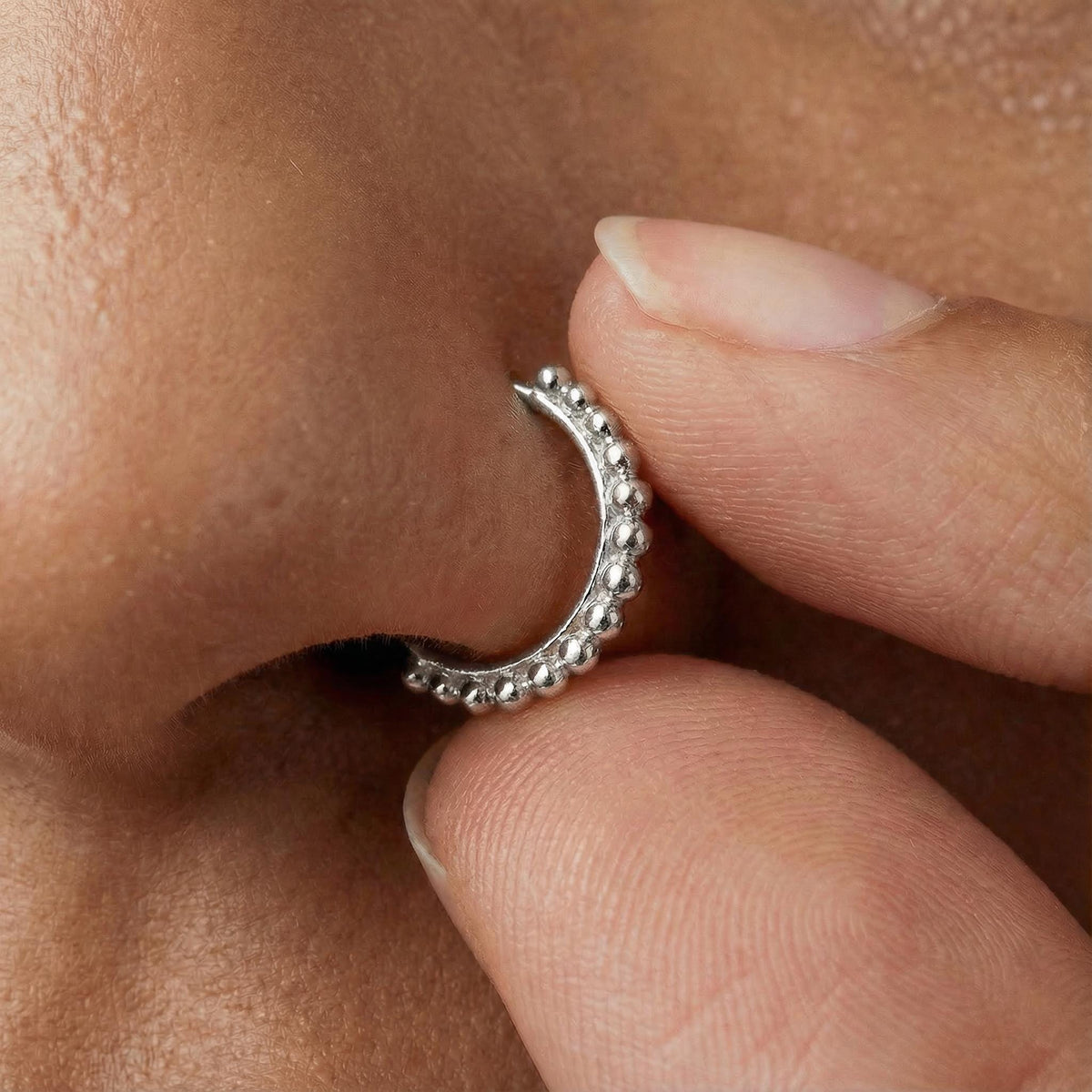 A close-up of a person's hand holding a silver hoop earring with a decorative design.