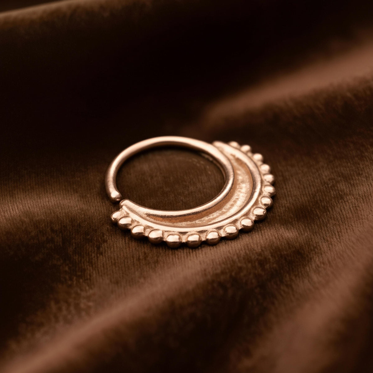 Nose Hoop Jewelry: A gold-colored metal ring with a decorative design rests on a brown fabric surface.