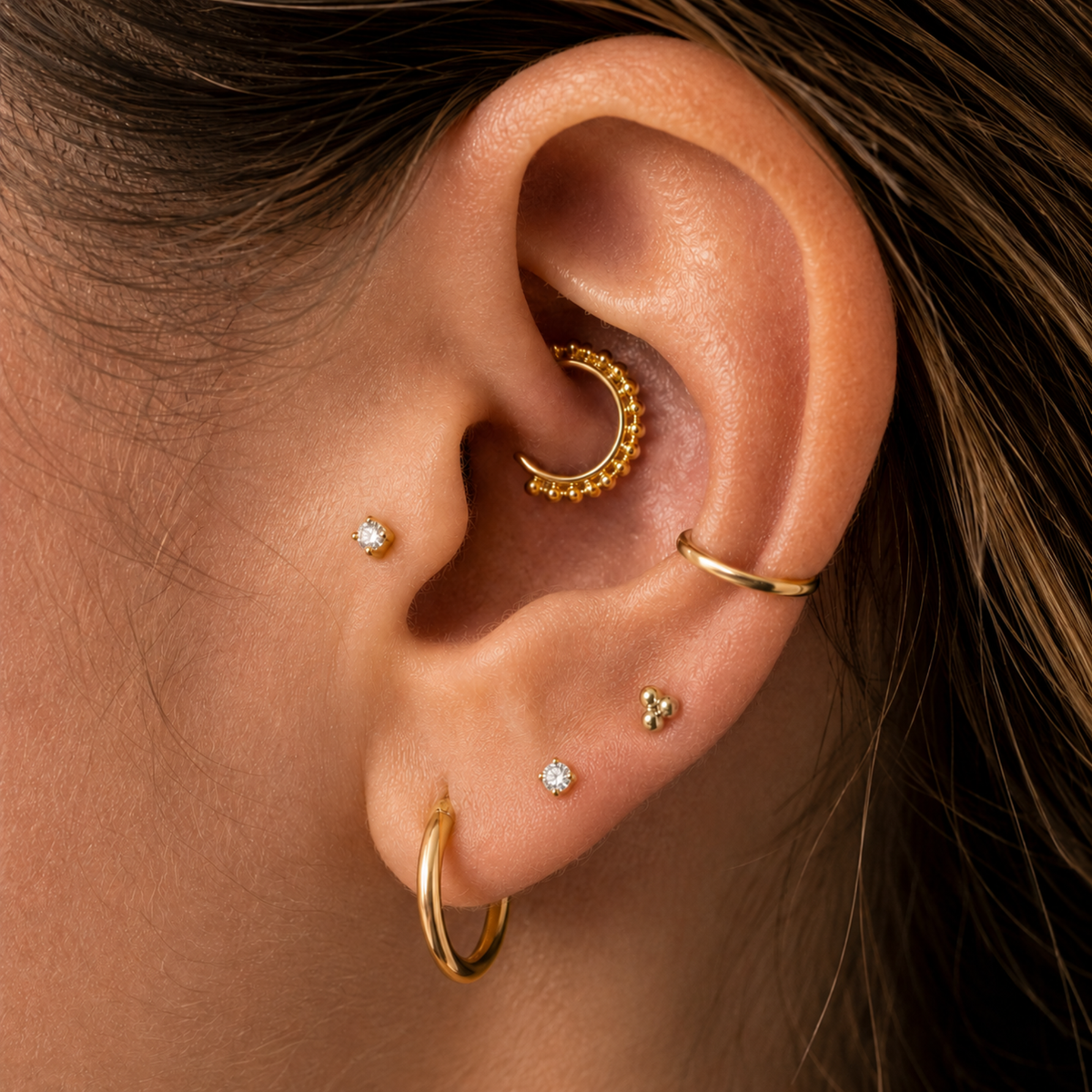 A close-up of a person's ear adorned with multiple gold earrings, including hoop earrings, studs, and a piercing.