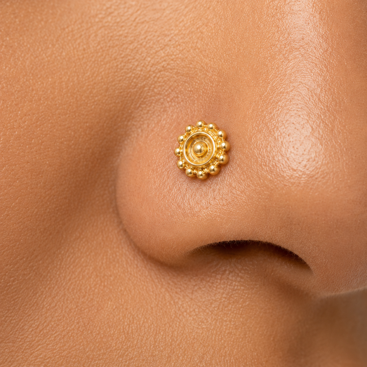 A close-up of a person's nose with a small, ornate gold nose ring.