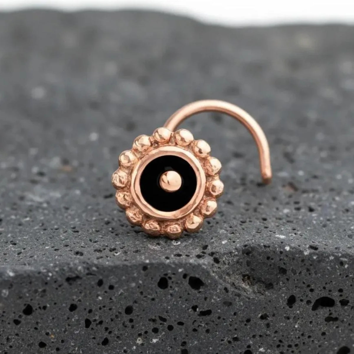 Nose Stud: A gold-colored nose ring with a black center is resting on a dark gray rock surface.