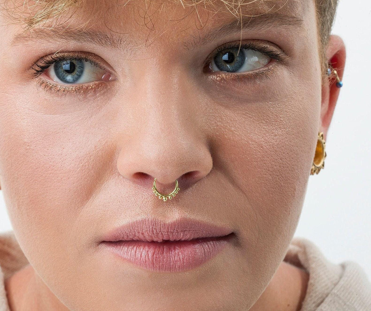 A close-up of a woman's face, with a nose ring and piercing, looking directly at the camera.