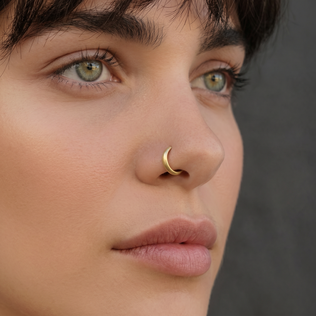 A close-up of a woman's face, focusing on her nose and lips, with a gold nose ring visible.