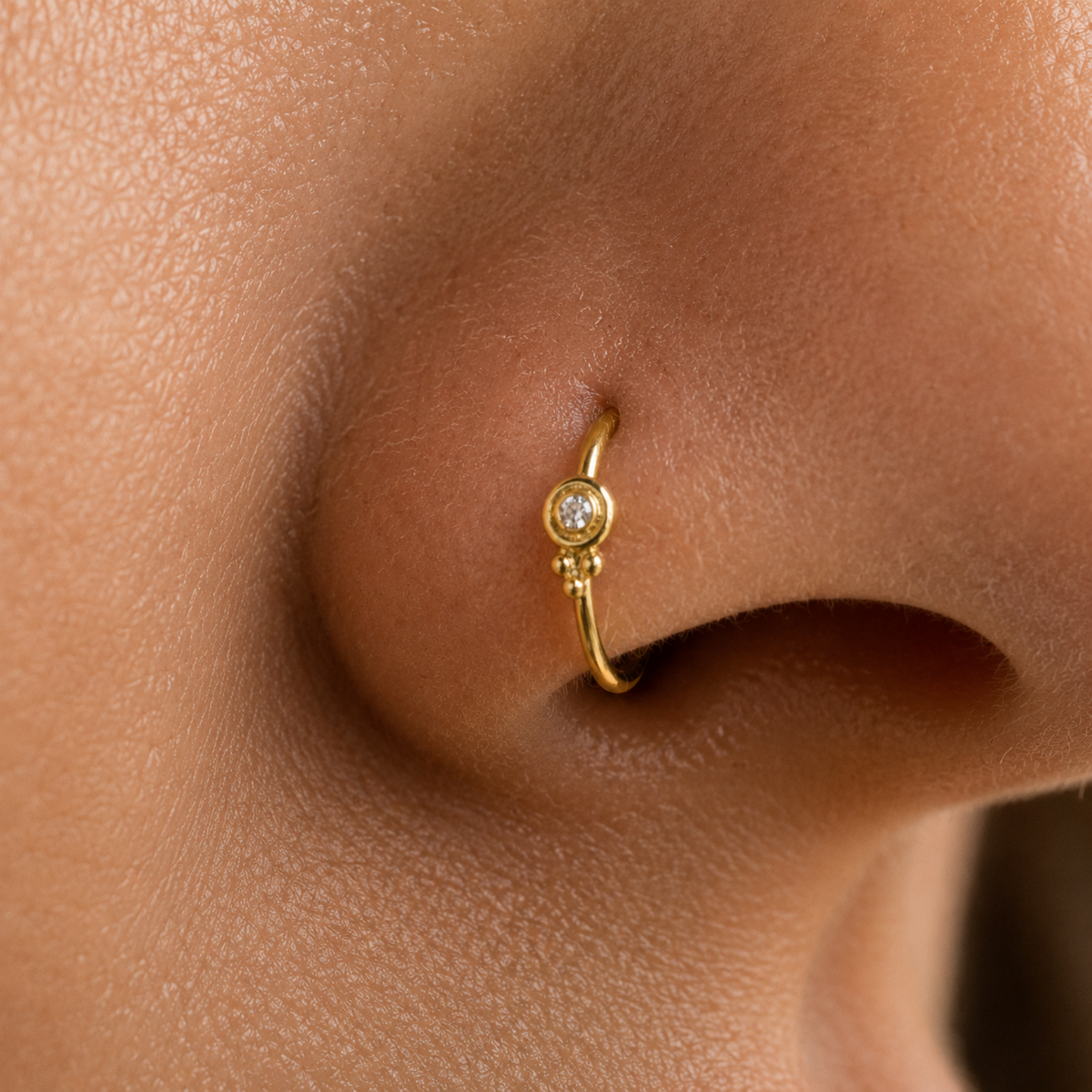 A close-up of a person's nose with a small gold nose ring featuring a diamond.